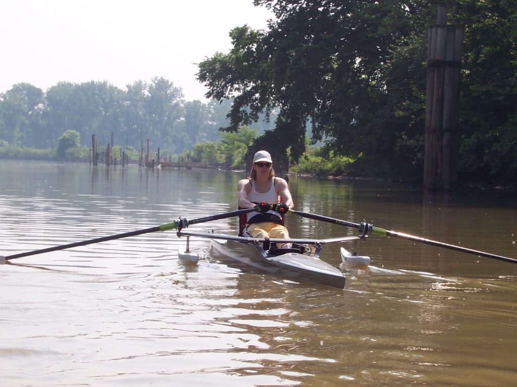 Jenny rows in a single scull on a river.